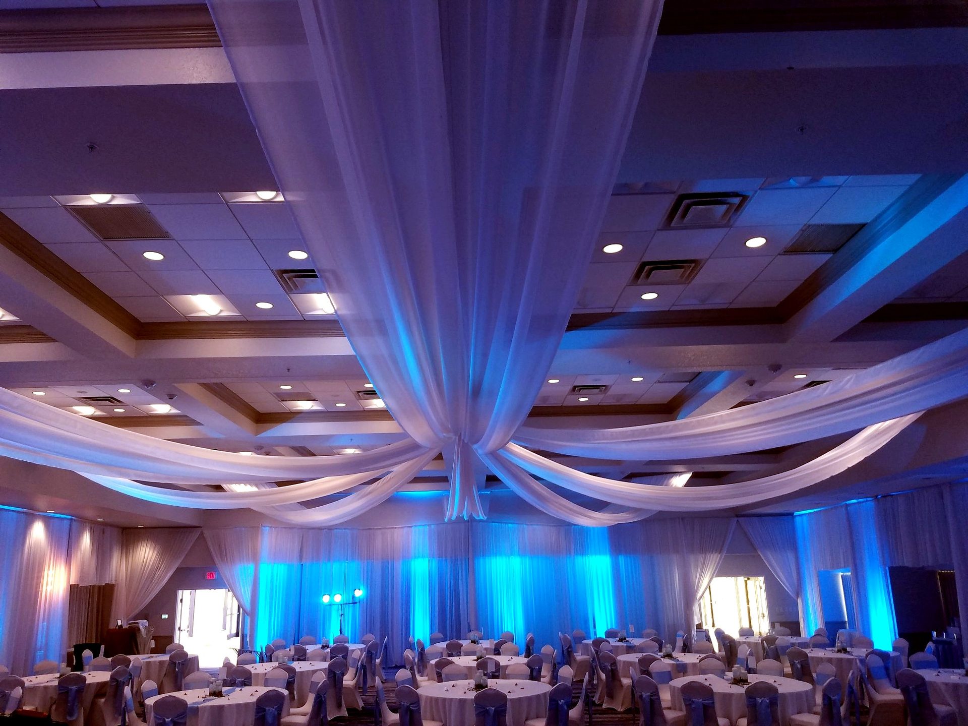 Ceiling drapery with blue uplighting — white ceiling swags and wall drape over a ballroom, by Altitude Event Design and Decor, Tampa Bay